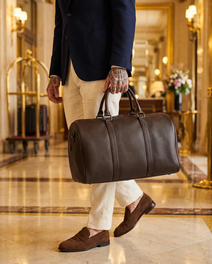 The Gstaad 44 leather travel bag in brown, carried through a hotel lobby