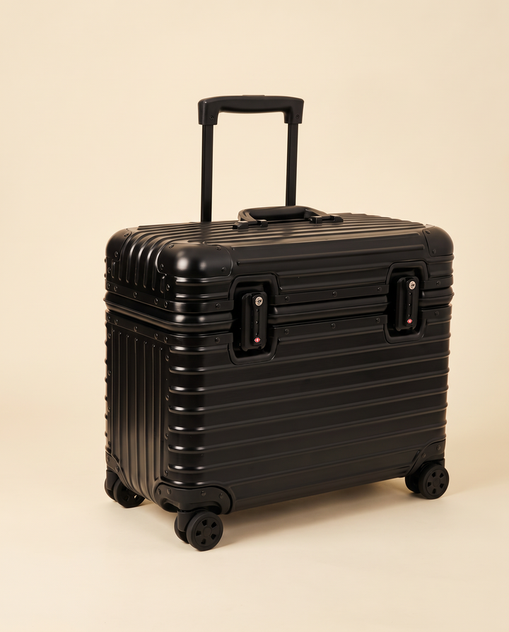 The Cap Ferrat 48 aluminum pilot case in black, three-quarter view on a cream studio backdrop